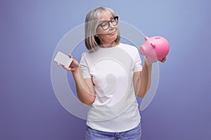 a woman of mature years with gray hair holds money capital from a piggy bank on a studio background with copy space