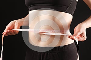 A woman measures the circumference of her abdomen on a black background. The concept of weight loss