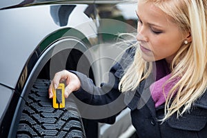 Woman measures tire tread of a car tire