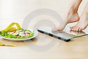 Woman measuring body weight on scales on salad background
