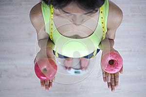 Woman measuring body weight on weighing scale holding donut and apple. Sweets are unhealthy junk food. Healthy eating , Lifestyle