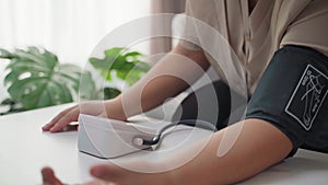 The woman is measuring her blood pressure using a portable blood pressure monitor