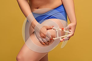 Woman measuring her body fat with caliper on yellow background