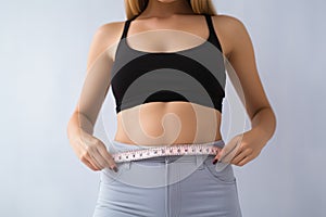 Woman measuring her waist on light background, closeup. Weight loss concept, Young slim woman measuring her body with a tape me,