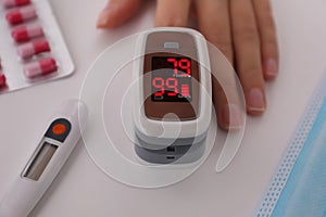 Woman measuring oxygen level with modern fingertip pulse oximeter at white table, closeup