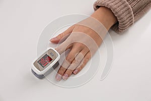 Woman measuring oxygen level with modern fingertip pulse oximeter at white table, top view