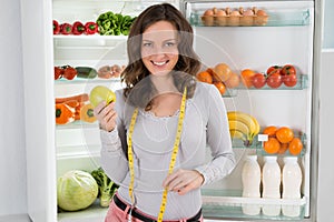 Woman With Measuring Tape And Apple Near The Refrigerator