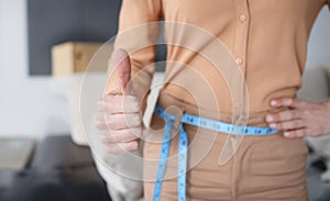 Woman with measuring tape at her waist showing thumb up closeup