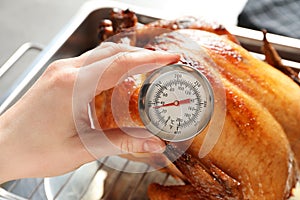 Woman measuring temperature of whole roasted turkey with meat thermometer