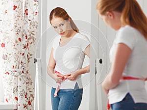 Woman measuring waist in front of mirror
