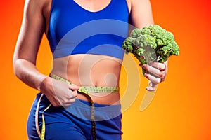Woman measuring waist and holding broccoli. People, fitness and healthcare concept