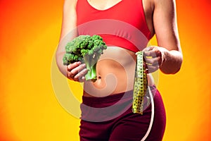 Woman measuring waist and holding broccoli. People, fitness and healthcare concept