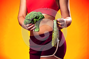 Woman measuring waist and holding broccoli. People, fitness and healthcare concept