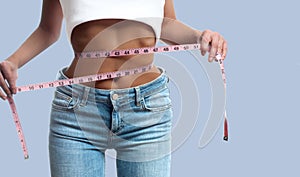 Woman is measuring waist after weight loss on pastel background