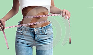 Woman is measuring waist after weight loss on pastel green background