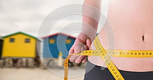 Woman measuring weight with measuring tape on waist near summer beach huts