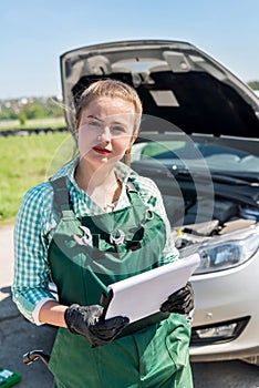 Woman mechanic with clipboard and broken car