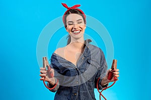 The woman mechanic holding jumper cables on the blue background.