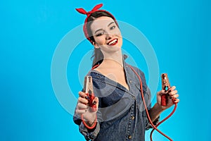 The woman mechanic holding jumper cables on the blue background.