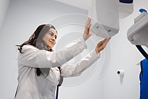 Woman in a medical coat adjusts a dental tomograph. Medical worker in the X-ray room.