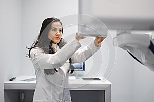 Woman in a medical coat adjusts a dental tomograph. Medical worker in the X-ray room.