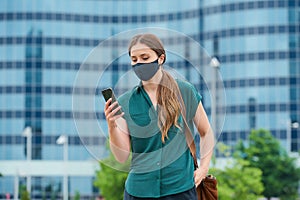 Woman in medical face mask using phone thrusting hand into a pocket of trousers