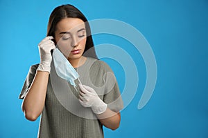 Woman in medical gloves putting on protective face mask against blue background. Space for text