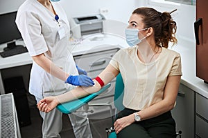 Woman in a medical mask being prepared for venipuncture