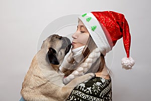 Woman in medical mask and Christmas hat kissing with pug dog. Coronavirus and Christmas