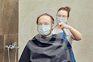 A woman in medical mask cuts a man hair with scissors in the bathroom close up. The concept of closed salons and barbershop during