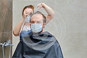 A woman in medical mask cuts a man`s hair with scissors, copy space