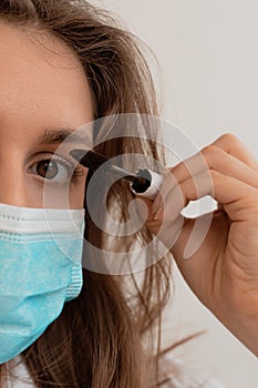 Woman in a medical mask does makeup, mascaras her eyes. The face of a young beautiful woman in a stylish mask