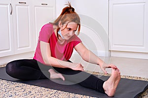 A woman in a medical mask does yoga sitting in a home kitchen, fitness is quarantined from coronavirus