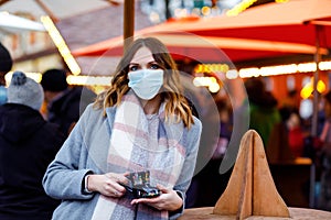 Woman with medical mask drinking hot punch, mulled wine on German Christmas market. People with masks as protection