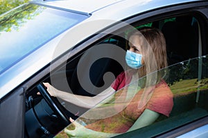 Woman in medical mask is driving the car. Coronavirus time. Dangerous situation