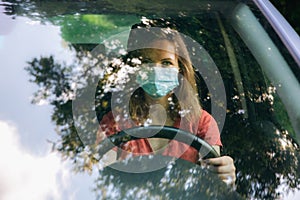 Woman in medical mask is driving the car. Coronavirus time. Dangerous situation