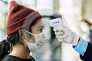 Woman in a medical mask getting her temperature measured by an electronic thermometer