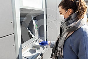 Woman in medical mask and glove with money at atm