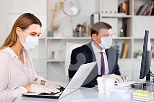 Woman in medical mask and gloves working on laptop in office