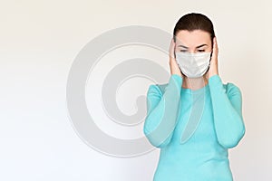 A woman in a medical mask grabbed her head in her hands and looks down. Shot on a white background.