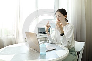 Woman in medical mask, hand sanitizer on the table, working with a laptop notebook, online learning education shopping