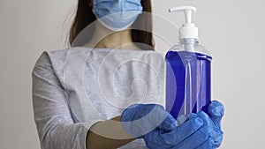 Woman with a medical mask and hands in latex glove holding bottle of alcohol gel