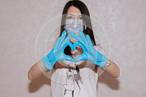 Woman with a medical mask and hands in latex glove shows the symbol of the heart. Doctor for the heart. Love to our