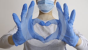 Woman with a medical mask and hands in latex glove shows the symbol of the heart. Doctor for the heart. Love to our pancreas.