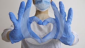 Woman with a medical mask and hands in latex glove shows the symbol of the heart. Doctor for the heart. Love to our pancreas.