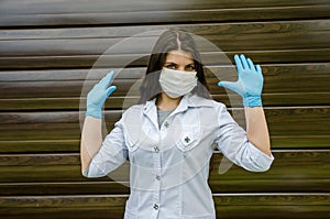Woman with a medical mask and hands in latex glove shows the symbol STOP. Stop the disease.