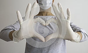 Woman with a medical mask and hands in latex white gloves shows the symbol of the heart. Doctor for the heart.