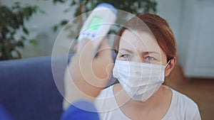 woman in a medical mask has his temperature measured with a digital covid 19 thermometer. coronavirus lockdown stay home
