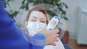 Woman in a medical mask has his temperature measured with a digital thermometer. Coronavirus lockdown stay home social