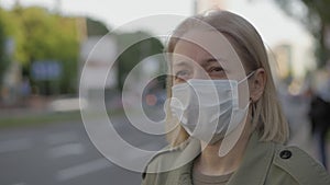 A woman in a medical mask on her face stands at a bus stop in the city centre